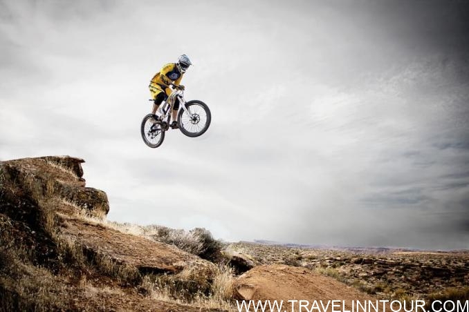 Mountain biker performing a jump on a rocky trail under a cloudy sky, highlighting Utah's outdoor adventure opportunities.