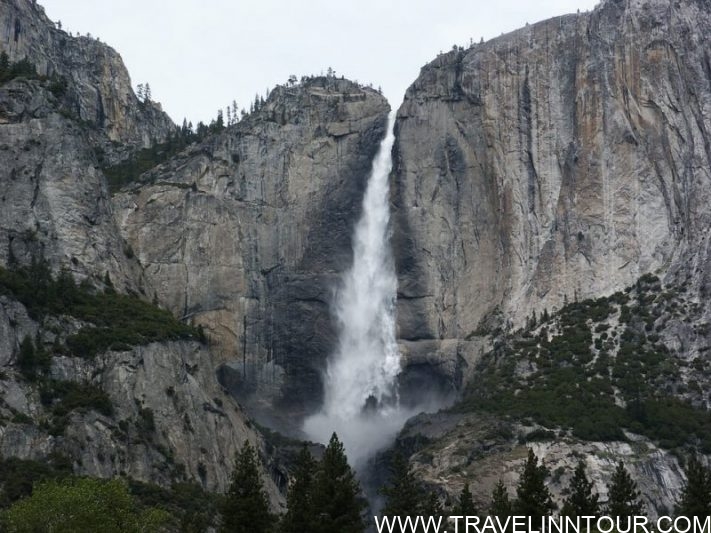Scenic view of Upper Yosemite Falls cascading down a rocky cliff surrounded by lush greenery in Yosemite National Park.