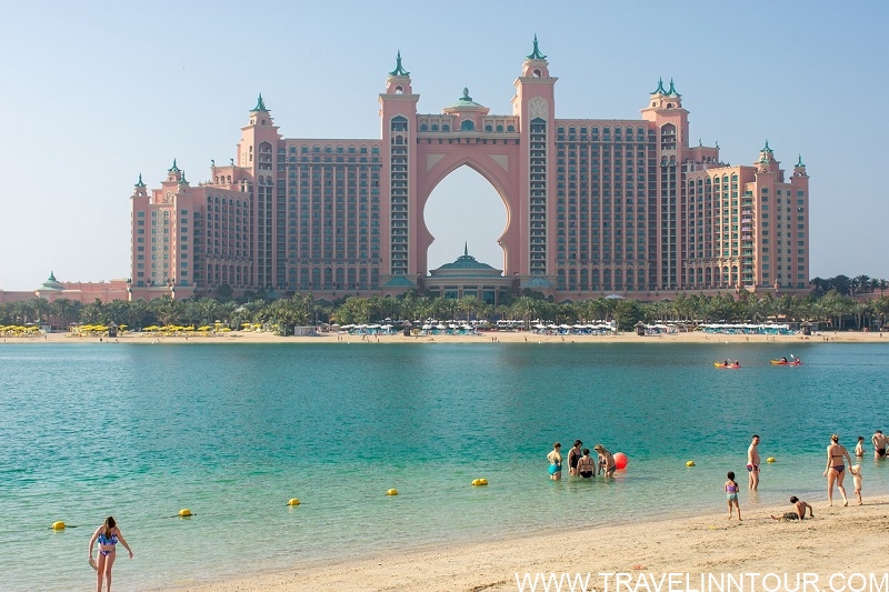 View of Atlantis The Palm from a beach in Dubai, with tourists enjoying the water and sandy shore, showcasing popular attractions for a 2-day Dubai itinerary.