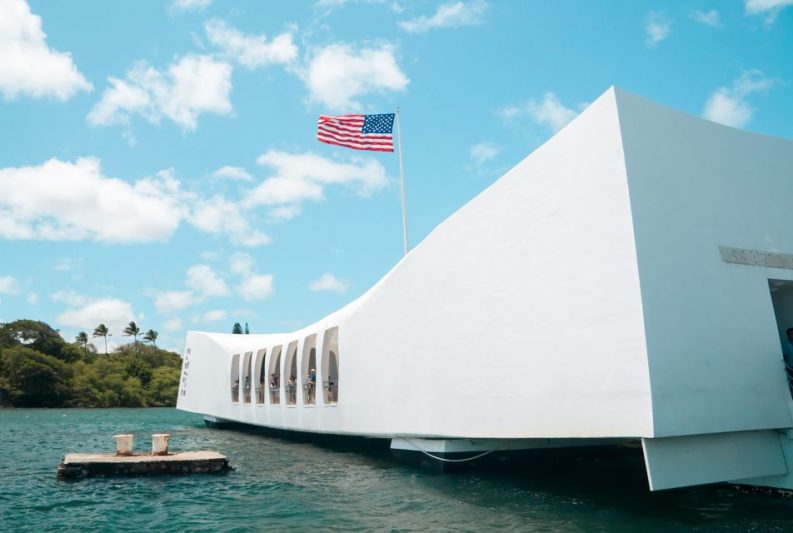 USS Arizona Memorial at Pearl Harbor in Hawaii with American flag flying, clear blue sky, and water view &ndash; a must-visit historic site in your tropical adventure guide.