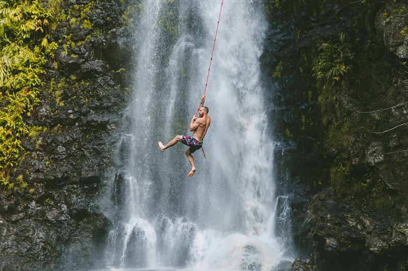 Person swinging on a rope in front of a tropical waterfall in Hawaii.