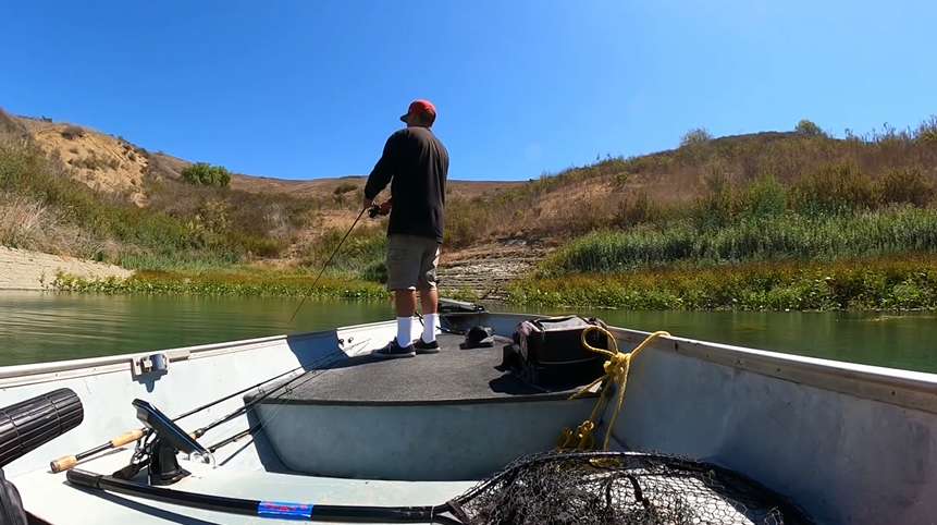 Angler fishing on a boat in a serene California lake, surrounded by dry hills and sparse vegetation, perfect for bass fishing tips and freshwater success.