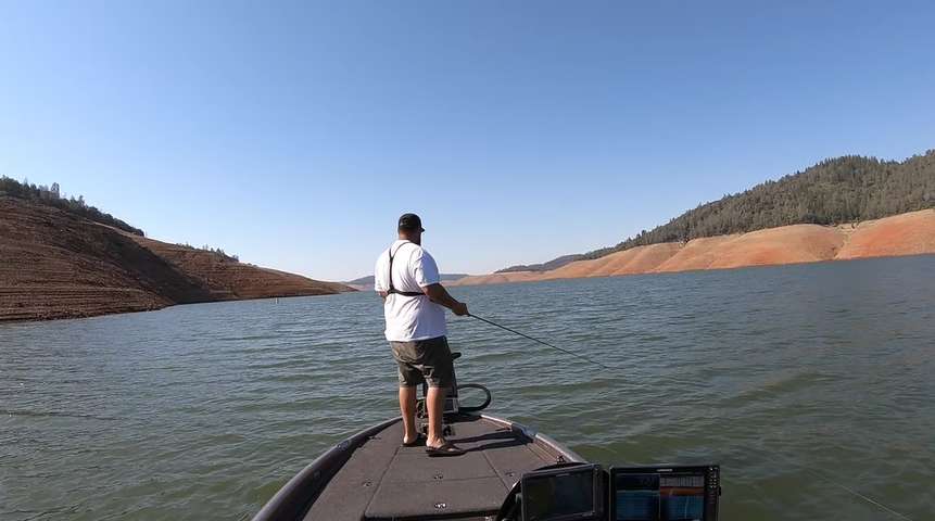 Angler fishing on a boat in a California freshwater lake surrounded by hills, focusing on bass fishing.