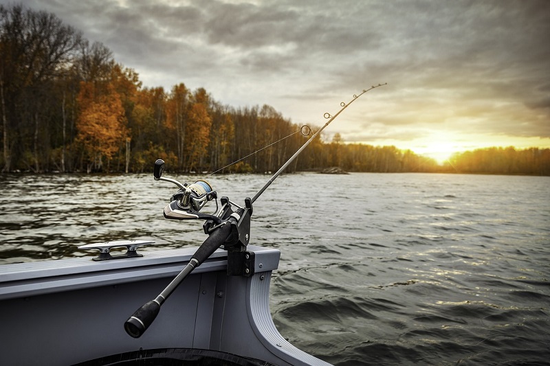 Fishing rod resting on a boat at sunrise on a lake, surrounded by autumn trees, ideal for California bass fishing tips and freshwater success.