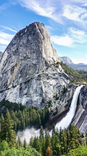 Impressive granite dome and waterfall in Yosemite National Park surrounded by dense forest and clear blue sky, showcasing popular hiking and natural attractions in the park.