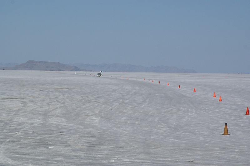 Car driving on the expansive Bonneville Salt Flats with orange cones marking the path, surrounded by distant mountains under a clear blue sky, highlighting outdoor adventures in Utah.