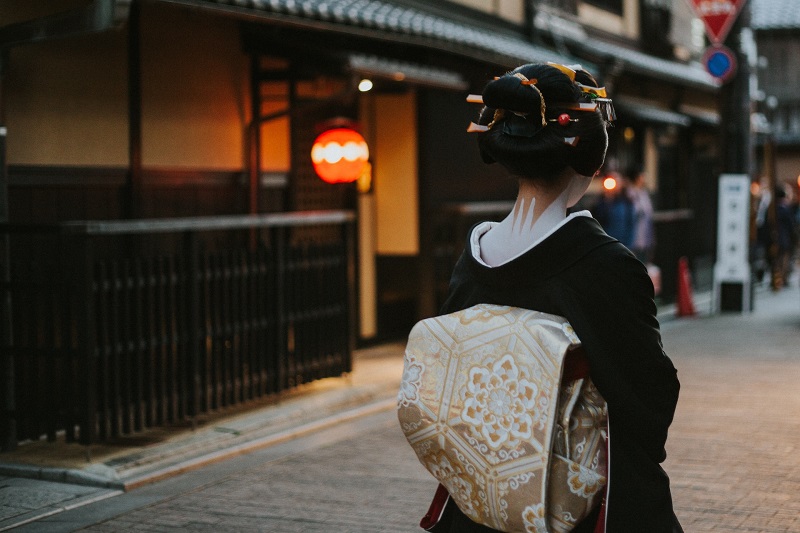 Traditional geisha walking through a dimly lit street in Kyoto, Japan, showcasing her ornate kimono and hairstyle, embodying the cultural essence of the city.