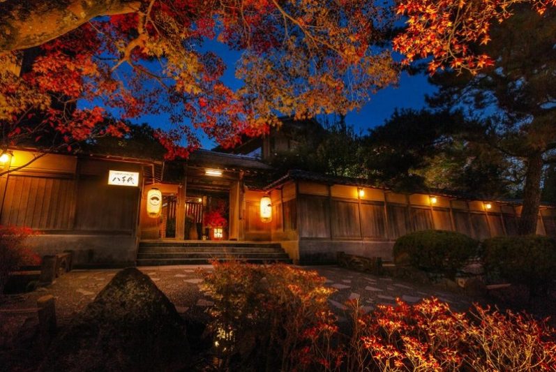 Traditional Kyoto house illuminated at night with vibrant red autumn leaves enhancing the serene atmosphere, showcasing the cultural beauty during a two-day itinerary in Kyoto.