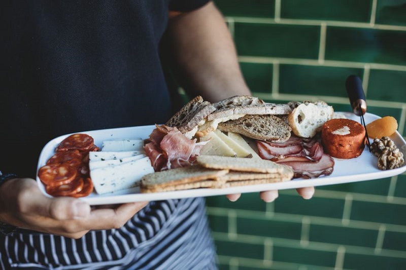 Person holding a platter with assorted Portuguese cheeses, cured meats, bread, and nuts, ideal for a Lisbon walking tour culinary experience.