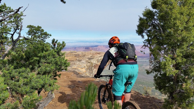 Mountain biker on a scenic trail in Utah, surrounded by lush greenery and panoramic views of distant canyons, exemplifying outdoor adventure.
