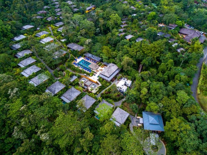 Aerial view of a resort in Costa Rica surrounded by lush greenery, with numerous villas and a central pool area, showcasing a serene and private setting for clothing o