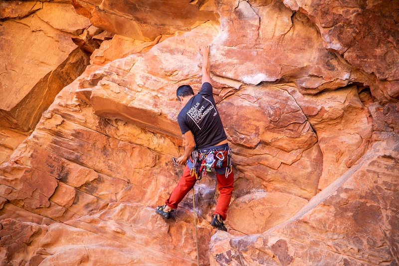 Climber ascending a red rock face in Utah, equipped with climbing gear, illustrating outdoor adventure opportunities.
