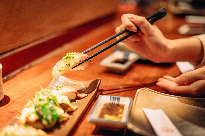 Close-up of a person using chopsticks to pick up a piece of sushi from a wooden platter in a Kyoto restaurant, showcasing local Japanese cuisine.