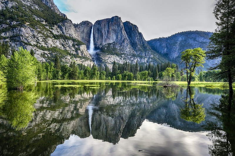 Scenic view of Yosemite National Park featuring a waterfall, granite cliffs, lush greenery, and a reflective lake, perfect for a 1-day hiking and travel adventure.