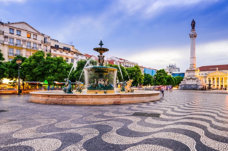 Lisbon's Rossio Square with ornate fountain, iconic patterned pavement, and historic architecture at dusk, highlighting city walking tours.