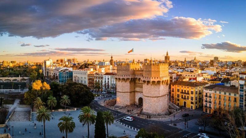 Aerial view of Valencia featuring historical architecture and palm trees at sunset, highlighting city attractions.