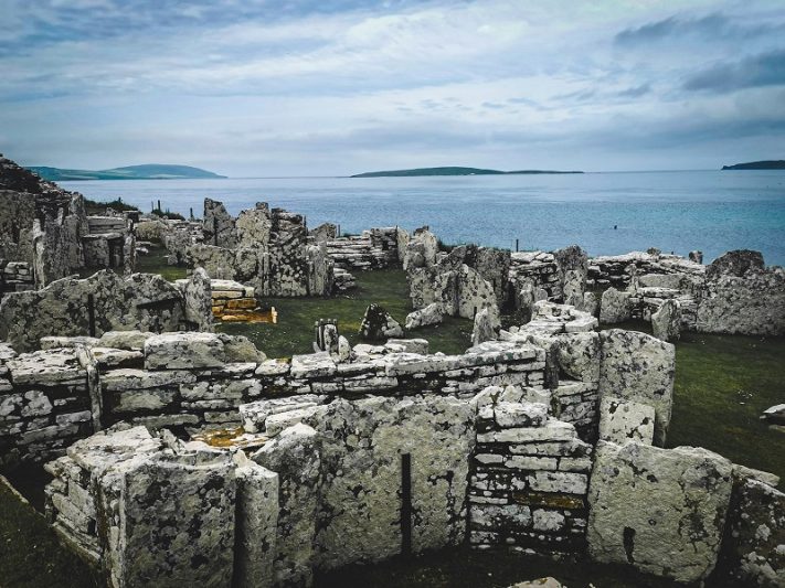 Ancient stone ruins on a Scottish island overlooking the sea, with distant islands visible under a cloudy sky, highlighting Scotland's historic and natural beauty for vacation explorers.
