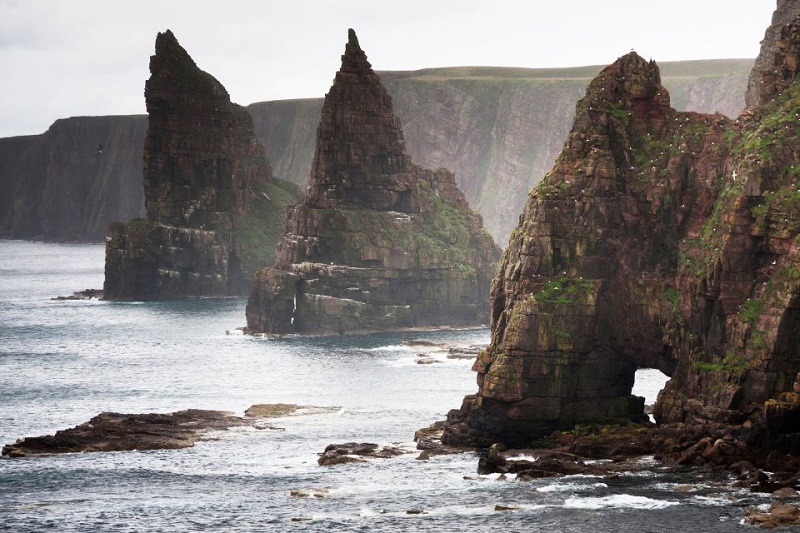 Dramatic sea stacks on the rugged coastline of a Scottish island, under a cloudy sky, showcasing natural rock formations and scenic ocean views.