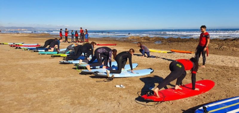Surfing lesson on a sandy beach in Valencia, Spain with people practicing on surfboards, highlighting Valencia's top seaside attractions.
