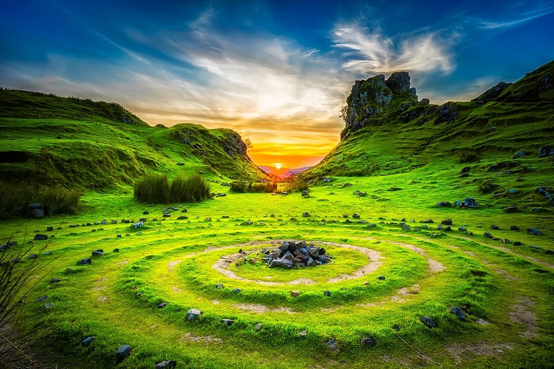 Beautiful landscape of a Scottish island at sunset with a vibrant green grassy terrain, featuring a spiral stone formation on the ground and rugged hills in the background, perfect setting for an island vacation.