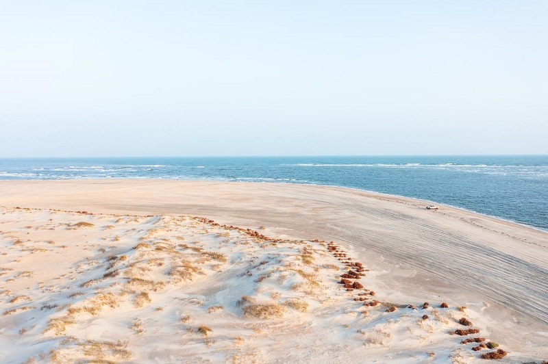 Aerial view of a serene beach on a Scottish island, featuring sandy dunes and the calm blue ocean under a clear sky, ideal for a perfect vacation.
