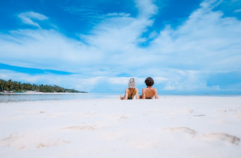 A couple relaxing on a pristine, secluded beach in Costa Rica, with clear blue skies and palm trees lining the horizon, highlighting natural beauty and tranquility.