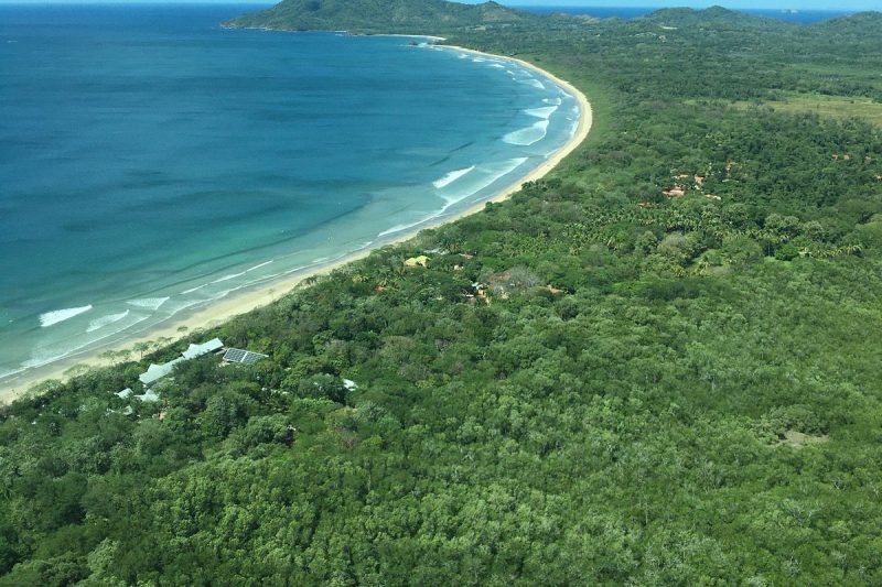 Aerial view of a secluded beach in Costa Rica with lush green forests meeting the clear blue ocean, ideal for discovering hidden spots.