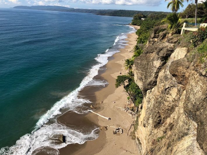 Scenic view of a secluded beach in Costa Rica with clear blue waters, rocky cliffs, and palm trees, ideal for discovering hidden nude beaches.