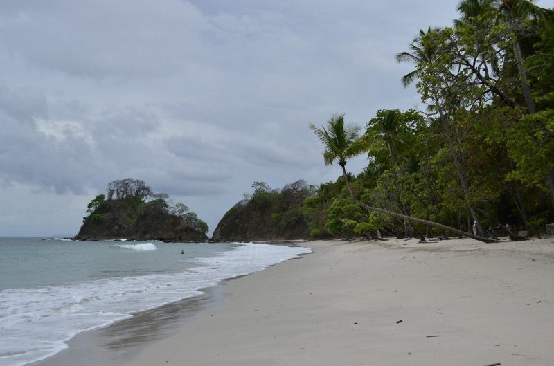 Secluded beach in Costa Rica with white sand, gentle waves, and lush greenery, ideal for nudist visitors seeking privacy.