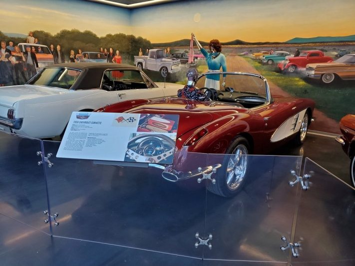 Classic cars displayed in a Texas museum with a vintage mural backdrop, featuring a red convertible with informational signage, highlighting Texas' rich automotive history and classic car collections.