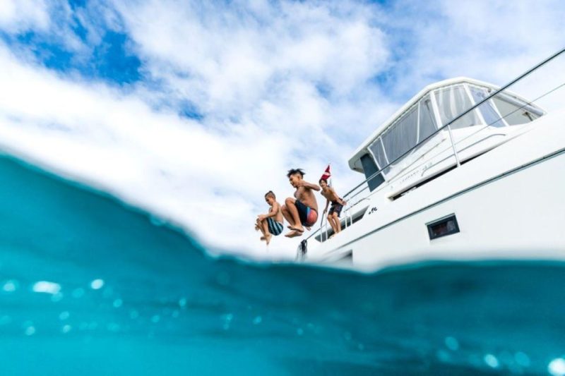 Three people jumping off a boat into the clear blue ocean, enjoying water activities in Kona, Hawaii against a cloudy sky.