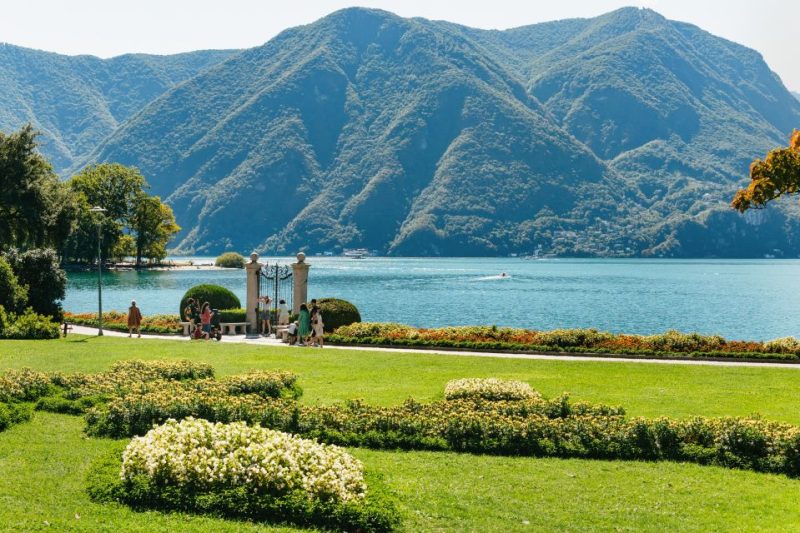 Scenic view of Lake Como in November with lush green gardens in the foreground and majestic mountains in the background, showcasing autumn travel appeal with fewer crowds.