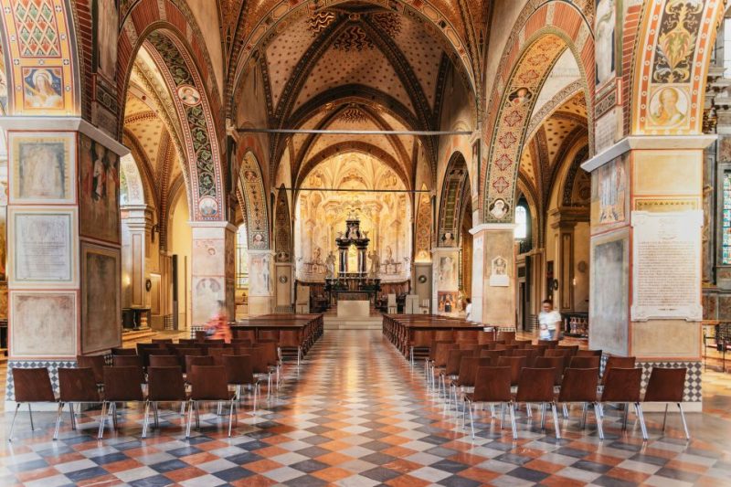 Interior of a historic church at Lake Como featuring ornate arches and frescoes, with empty wooden chairs and a serene atmosphere, highlighting cultural exploration during quieter November months.