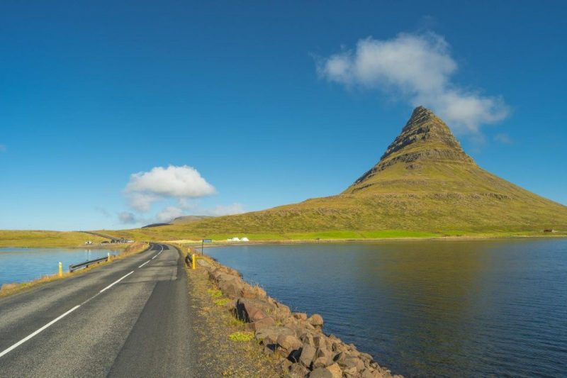 Scenic view of Kirkjufell mountain with clear blue sky and a road by the water in Iceland