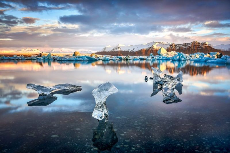 Scenic view of Iceland's Jokulsarlon Glacier Lagoon with floating icebergs under a vibrant sunset sky, highlighting the natural beauty of Iceland's landscapes.