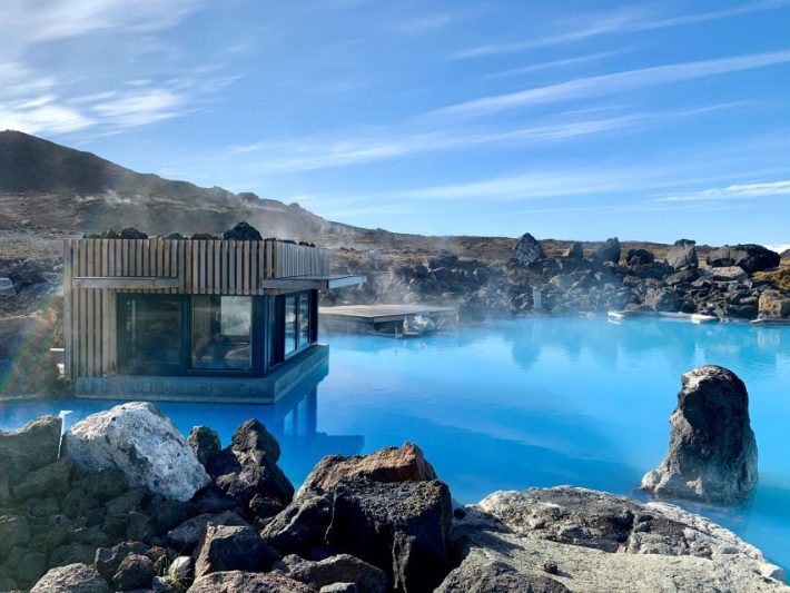 Geothermal spa with steaming blue water surrounded by volcanic rocks in Iceland, showcasing a natural and serene setting under a clear sky.