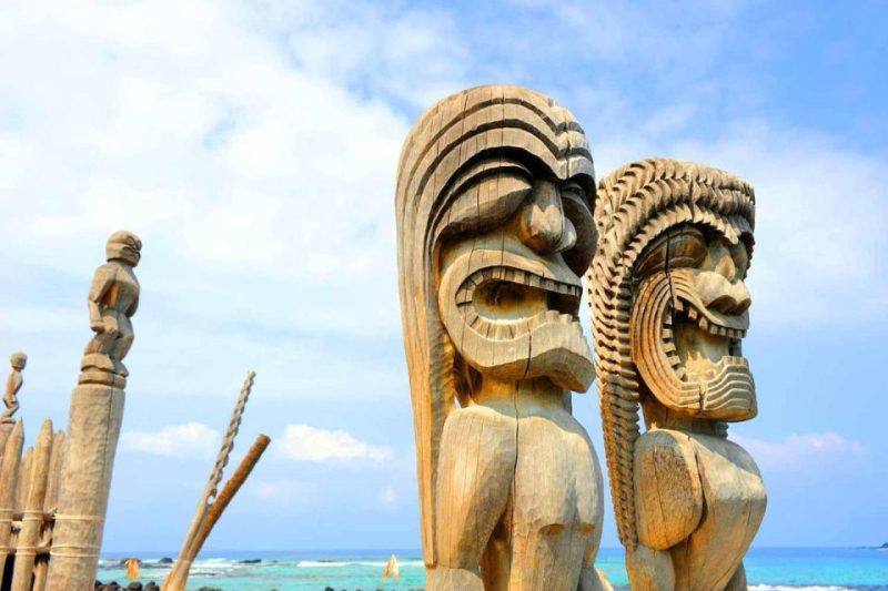 Traditional Hawaiian wooden statues overlooking the ocean at Pu'uhonua o Hōnaunau National Historical Park, a popular cultural attraction in Kona, Hawaii.