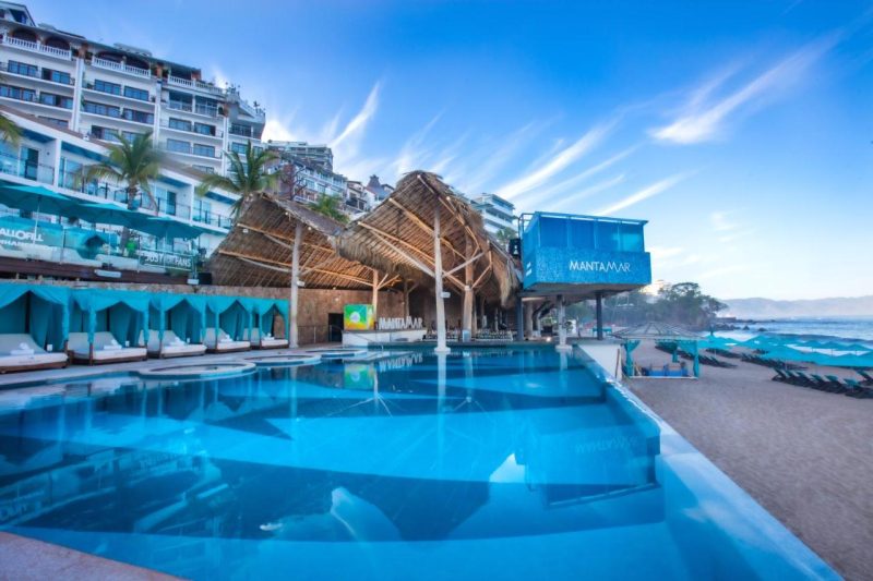 Beachfront view of Mantamar in Puerto Vallarta, featuring a luxurious pool area with cabanas, modern architecture, and clear blue skies.