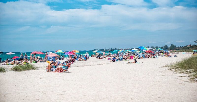 Beachgoers enjoying a sunny day at a Sarasota beach with colorful umbrellas and clear blue skies, highlighting its appeal as a family-friendly destination in Florida.