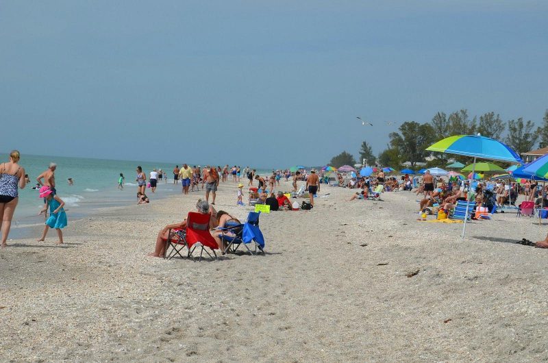 Crowded Sarasota beach with families enjoying the sun, colorful umbrellas, and calm ocean waves in Florida.