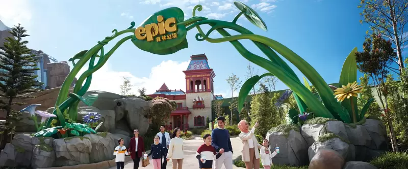 Family enjoying a day at Genting SkyWorlds Theme Park in Malaysia, walking under the decorative 'Epic' entrance with large green leaves and flowers, perfect for a short vacation getaway.